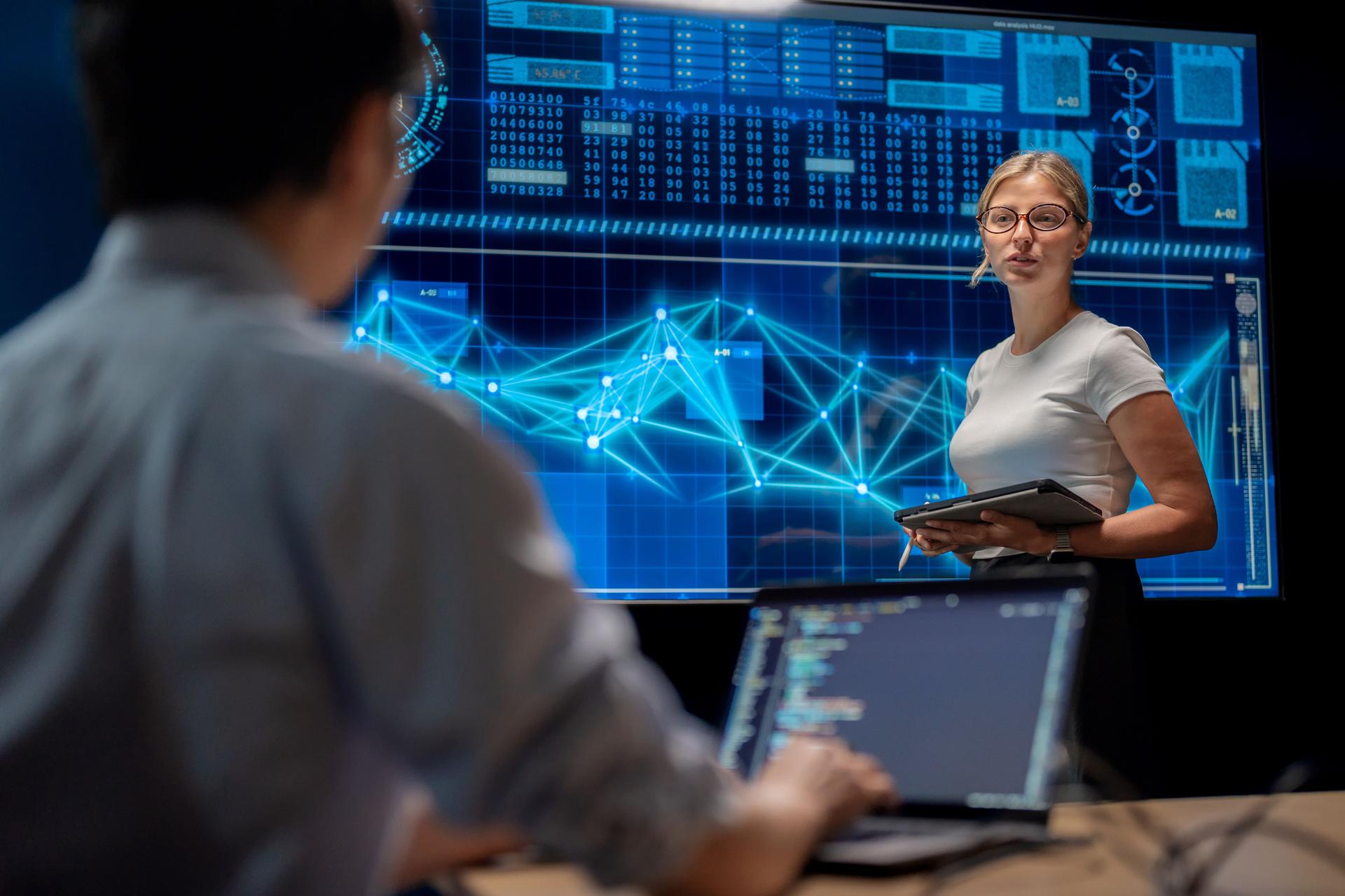Female employee presenting data science charts on screen in meeting room. Corporate teamwork, communication, brainstorming, AI, coding, technology, finance strategy, and innovation for business achievement.
